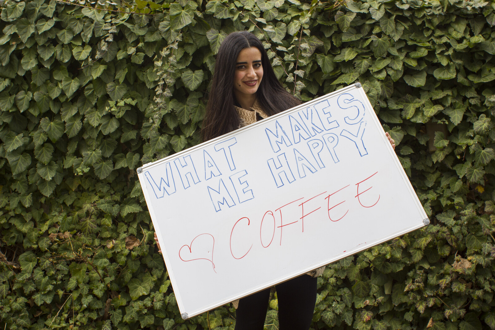 Frau hält ein Schild hoch mit der Aufschrift "#whatmakesmehappy". Kaffee macht sie glücklich