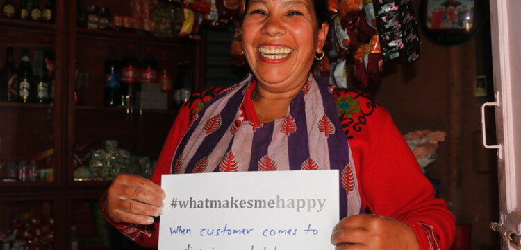 Frau hält in Nepal einen Zettel in einem Laden. Auf dem Zettel steht "whatmakesmehappy" und sie macht es glücklich, wenn Sie kunden im Geschäft hat.