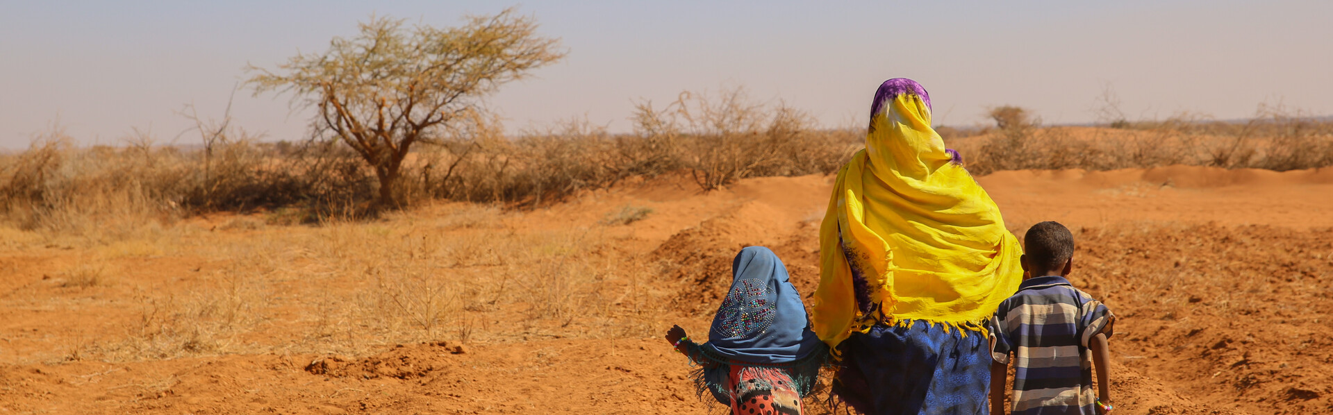 Eine Frau mit Kopftuch spaziert mit ihren zwei Kindern über ein ausgetrocknetes Feld in Somalia Eine Frau mit Kopftuch spaziert mit ihren zwei Kindern über ein ausgetrocknetes Feld in Somalia