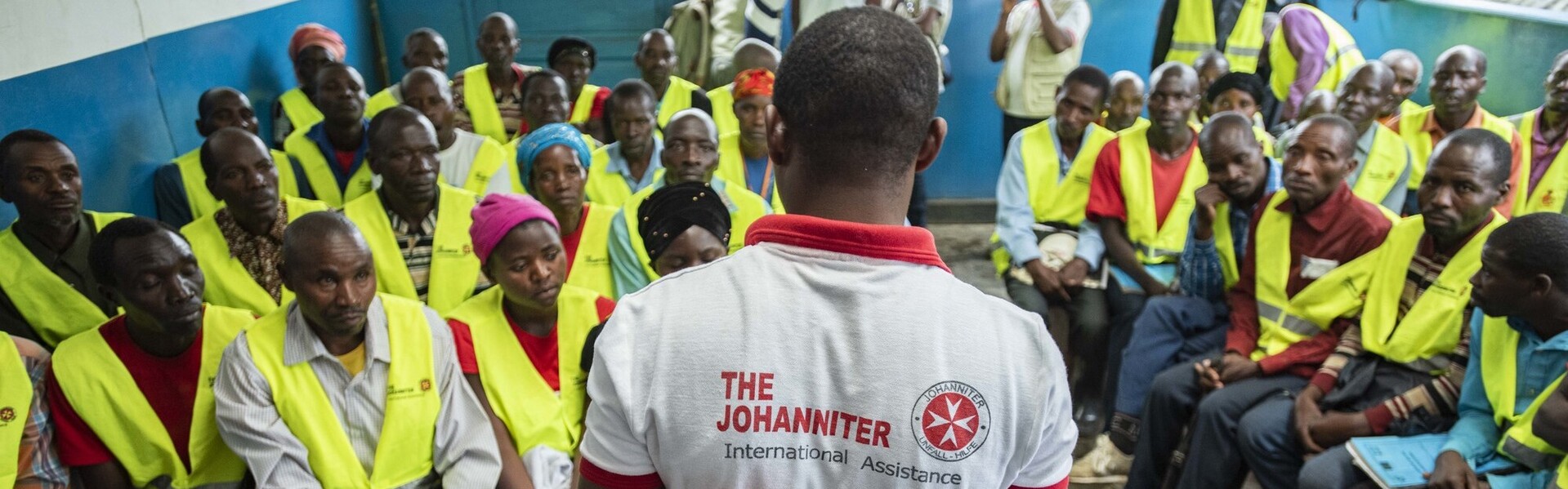 Ein Helfer der Johanniter spricht vor einer Gruppe von Menschen im Kongo Ein Helfer der Johanniter spricht vor einer Gruppe von Menschen im Kongo