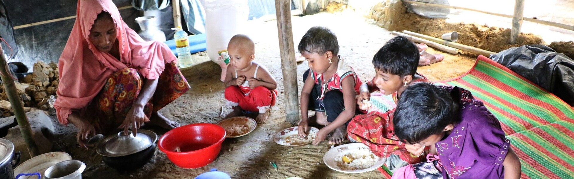 Eine Frau und vier Kinder sitzen zum Essen auf dem Boden Eine Frau und vier Kinder sitzen zum Essen auf dem Boden