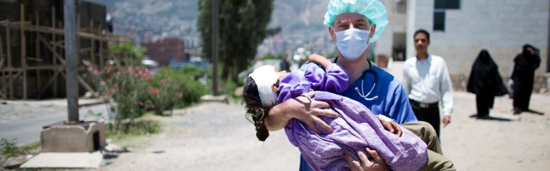 Durch fehlende Spenden kommt es im Jemen zunehmend zu einer humanitären Notlage Ein Arzt mit Mundmaske und Haube trägt ein Kind auf den Armen