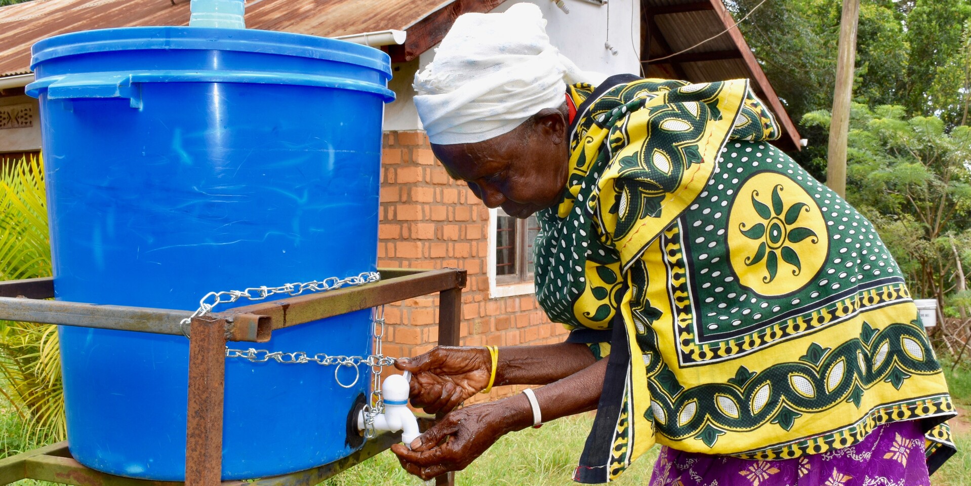 Eine ältere Frau in Tansania wäscht sich die Hände an einem Wassertank Eine ältere Frau in Tansania wäscht sich die Hände an einem Wassertank