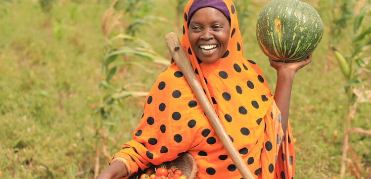 Eine Frau steht in Somalia mit frisch geerntetem Obst und Gemüse auf dem Feld