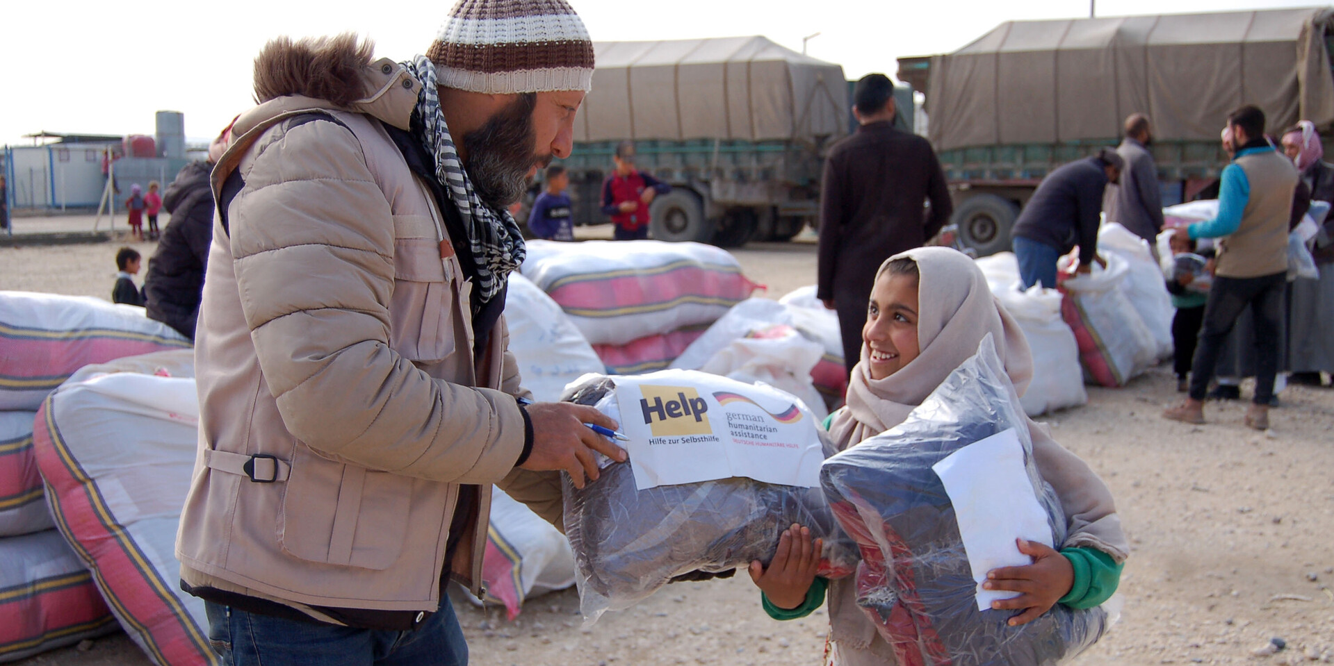 Ein Helfer überreicht einem Mädchen ein Hilfspaket in einem Flüchtlingscamp in Syrien Ein Helfer überreicht einem Mädchen ein Hilfspaket in einem Flüchtlingscamp in Syrien