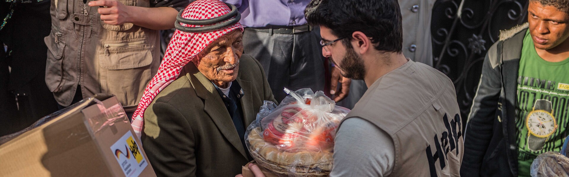 Flüchtlingshilfe in Jordanien: Ein Helfer übergibt Hilfsgüter an einen alten Mann Flüchtlingshilfe in Jordanien: Ein Helfer übergibt Hilfsgüter an einen alten Mann