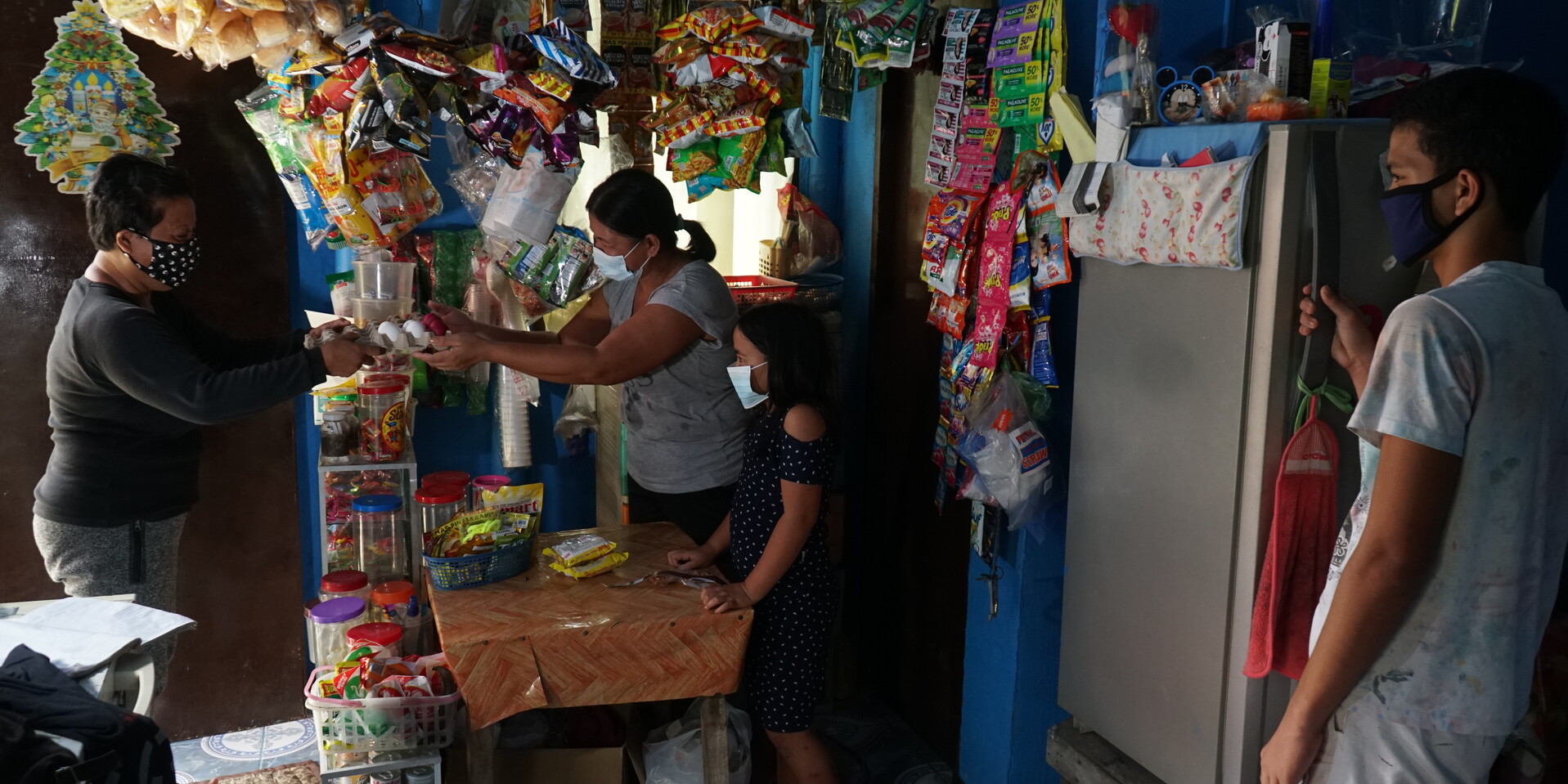 Eine Frau verkauft Lebensmittel in ihrem Kiosk in Bonbon Village an andere Bewohner:innen Eine Frau verkauft Lebensmittel in ihrem Kiosk in Bonbon Village an andere Bewohner:innen