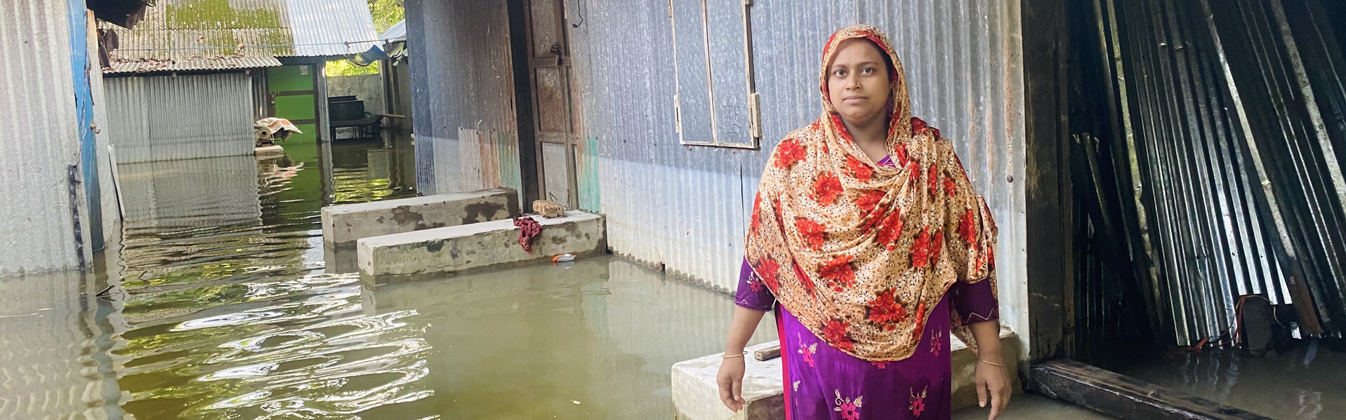 Der Monsun hat das Haus einer Frau in Bangladesch unterspült Eine Frau in Bangladesch steht im knietiefen Wasser
