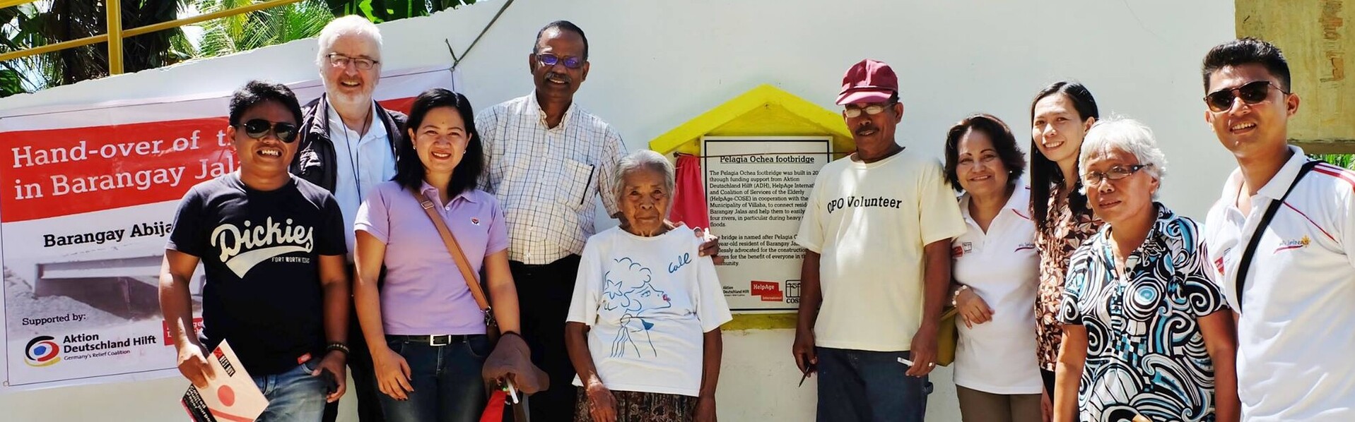 Helfer und Pelgia Olchea stehen zusammen vor der neu eingeweihten Brücke auf den Philippinen. Helfer und Pelgia Olchea stehen zusammen vor der neu eingeweihten Brücke auf den Philippinen.
