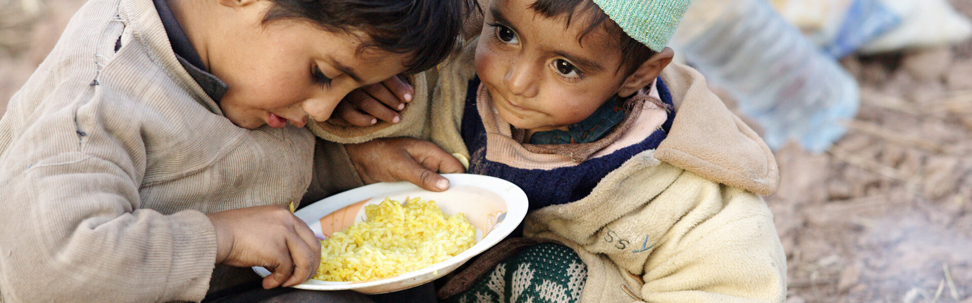 Zwei kleine Kinder teilen sich eine Schüssel Reis. Zwei Tage gegen Hunger und Armut